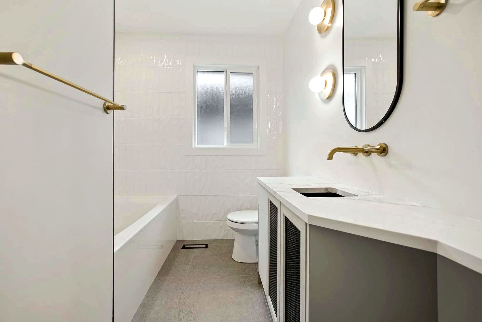 Renovated Sherwood Park bathroom with tiled tub surround, brass fixtures and a wall-mounted vanity